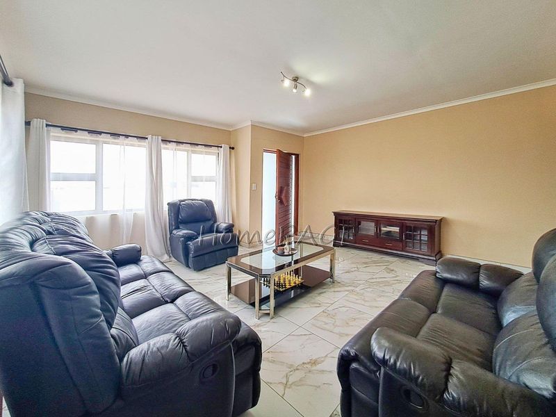 A spacious living room featuring polished marble-look floor tiles, neutral wall tones, and large windows providing ample natural light.