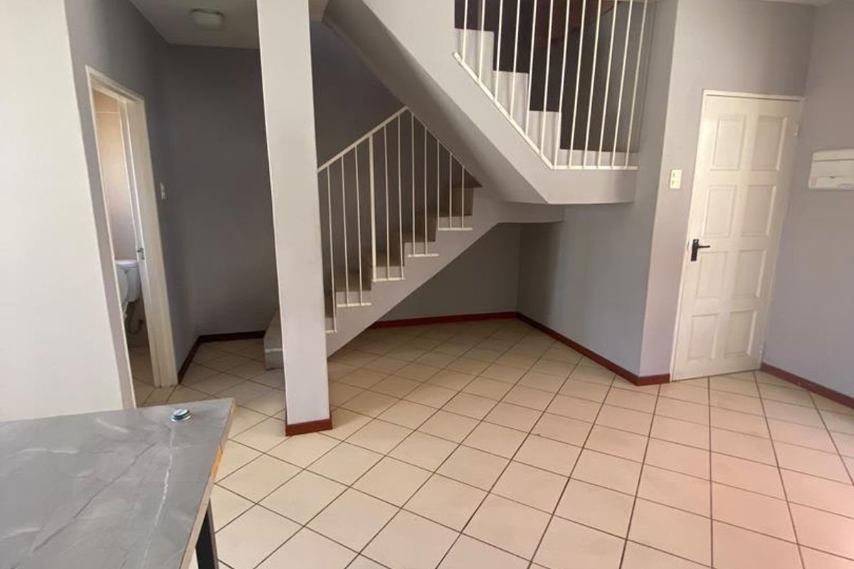 An open-plan living area featuring ceramic floor tiles and a central staircase with a metal balustrade, providing a clean and neutral foundation.