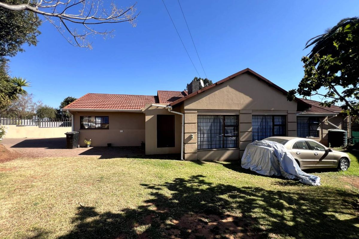 Rear view of the house featuring a tiled roof, paved driveway area, and established lawn with security bars on the windows.