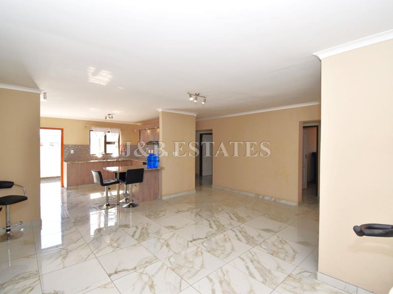 Spacious open-plan living area featuring polished marble-look floor tiles, a modern kitchen peninsula, and neutral wall finishes throughout.