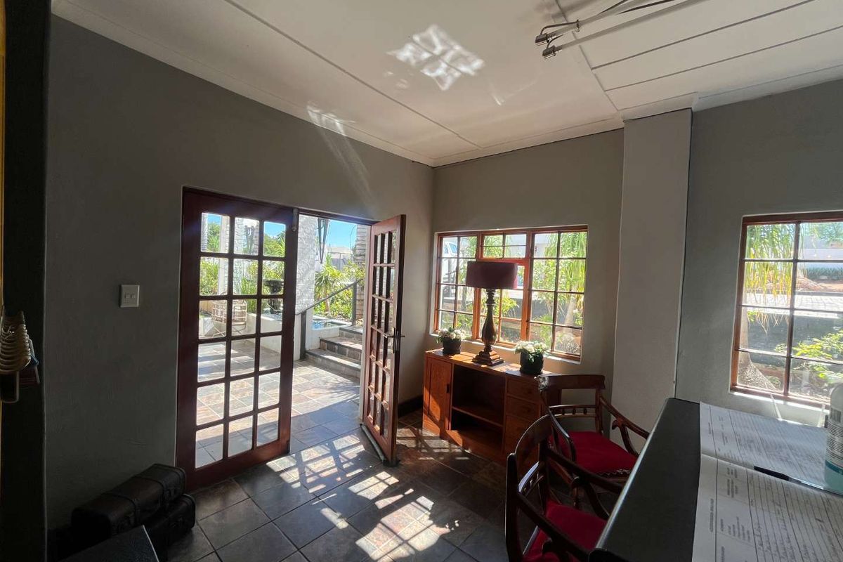 A bright living area featuring tiled flooring, wooden-framed windows, and double doors providing direct access to an outdoor patio space.