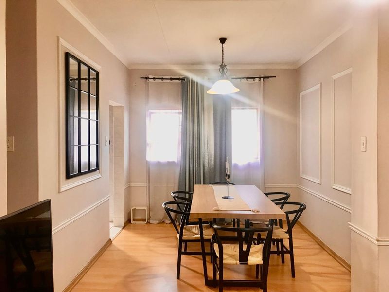 A well-lit dining room featuring laminate flooring, decorative wall molding, and a central pendant light fixture.