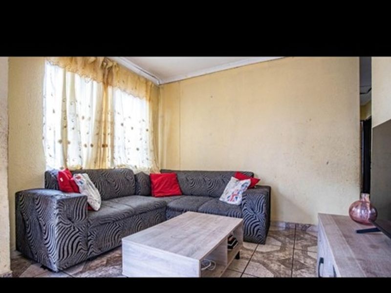 A living room featuring tiled flooring and cornicing, currently showing signs of wear on the wall surfaces.