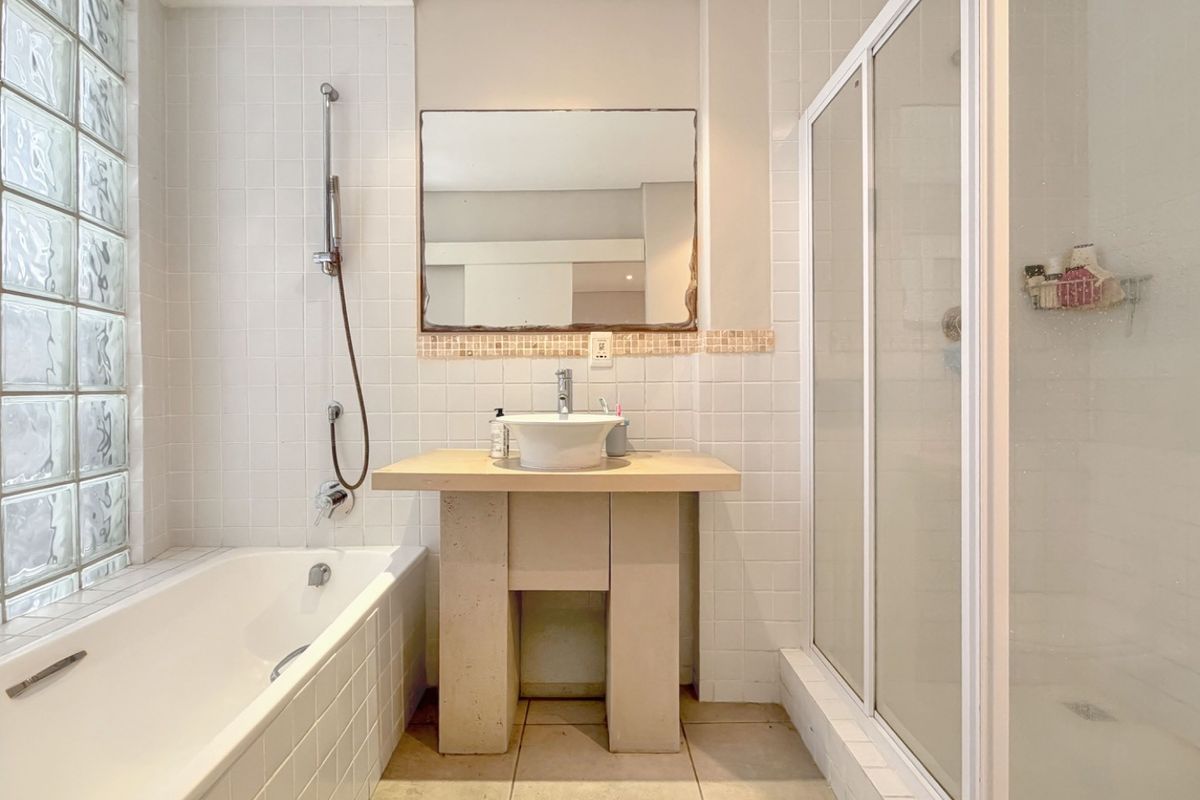 A functional bathroom featuring a built-in bathtub, separate shower enclosure, and a pedestal vanity with a vessel sink, accented by a glass block window.