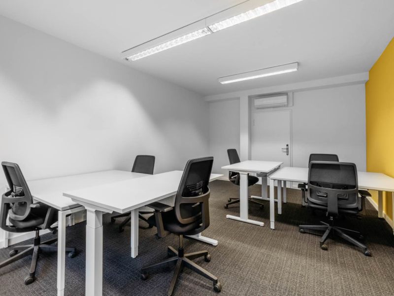 A clean, modern office space featuring carpeted flooring, recessed lighting, and a wall-mounted air conditioning unit.