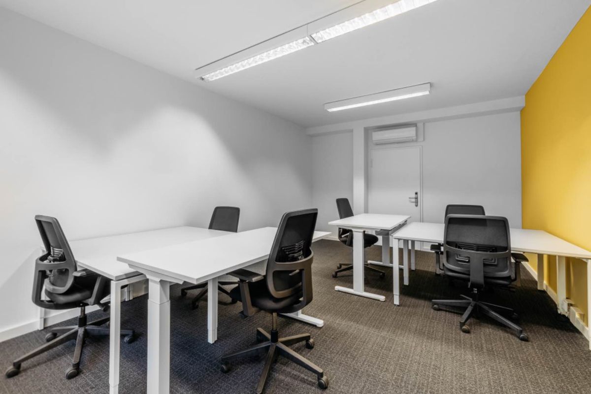 A clean, modern office space featuring carpeted flooring, recessed lighting, and a wall-mounted air conditioning unit.