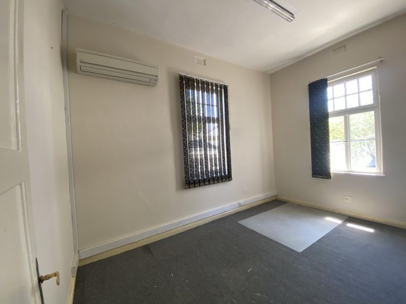 A vacant office space featuring split-system air conditioning, large windows with vertical blinds, and carpeted flooring, suitable for a professional workspace.