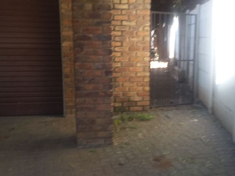 A view of a garage exterior featuring a roller shutter door, brick pillar, and paved driveway area with a side gate.