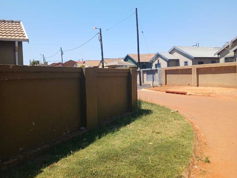 A street view showing the perimeter wall of the property, adjacent grass verge, and local road infrastructure.