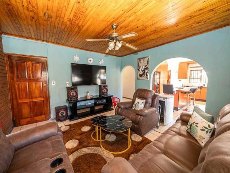 Open plan living area featuring a timber ceiling, ceiling fan, and arched access to the kitchen, with tiled flooring throughout.