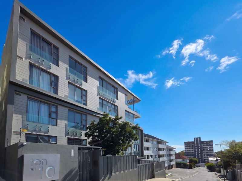 Modern multi-story penthouse apartment building exterior featuring contemporary glass balustrades, clean architectural lines, and secure perimeter fencing.