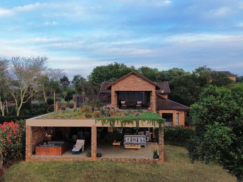 Aerial view of a brick house featuring a covered patio, integrated hot tub, and a unique green roof design set within a landscaped garden.