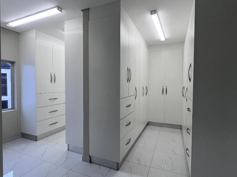 A modern, spacious walk-in dressing area featuring extensive white built-in cabinetry and polished marble-look floor tiles.