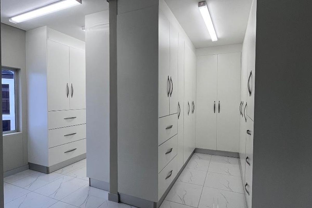 A modern, spacious walk-in dressing area featuring extensive white built-in cabinetry and polished marble-look floor tiles.