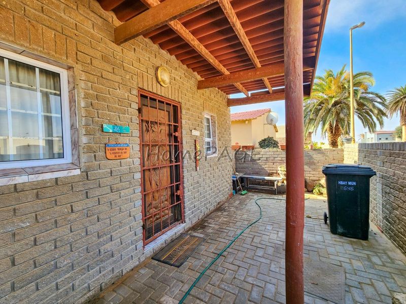 A covered outdoor patio area featuring brick construction, a timber pergola, and paved flooring, providing a functional space for outdoor living.