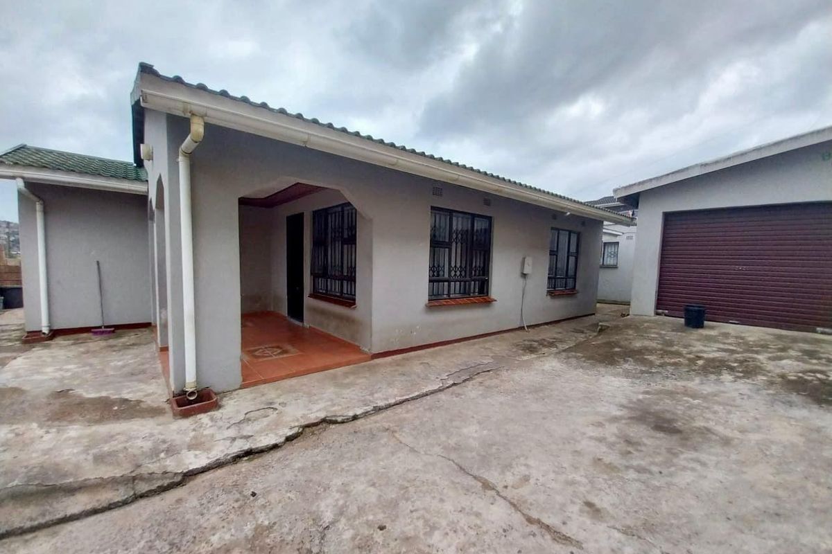 Rear view of the property featuring a covered patio, concrete driveway, and a detached garage with a roller door.