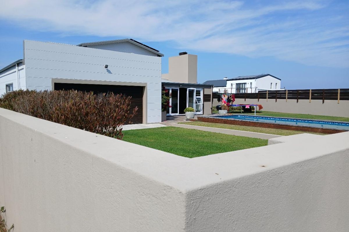 Rear view of the property featuring a swimming pool, landscaped lawn, and modern exterior facade with a garage and patio access.