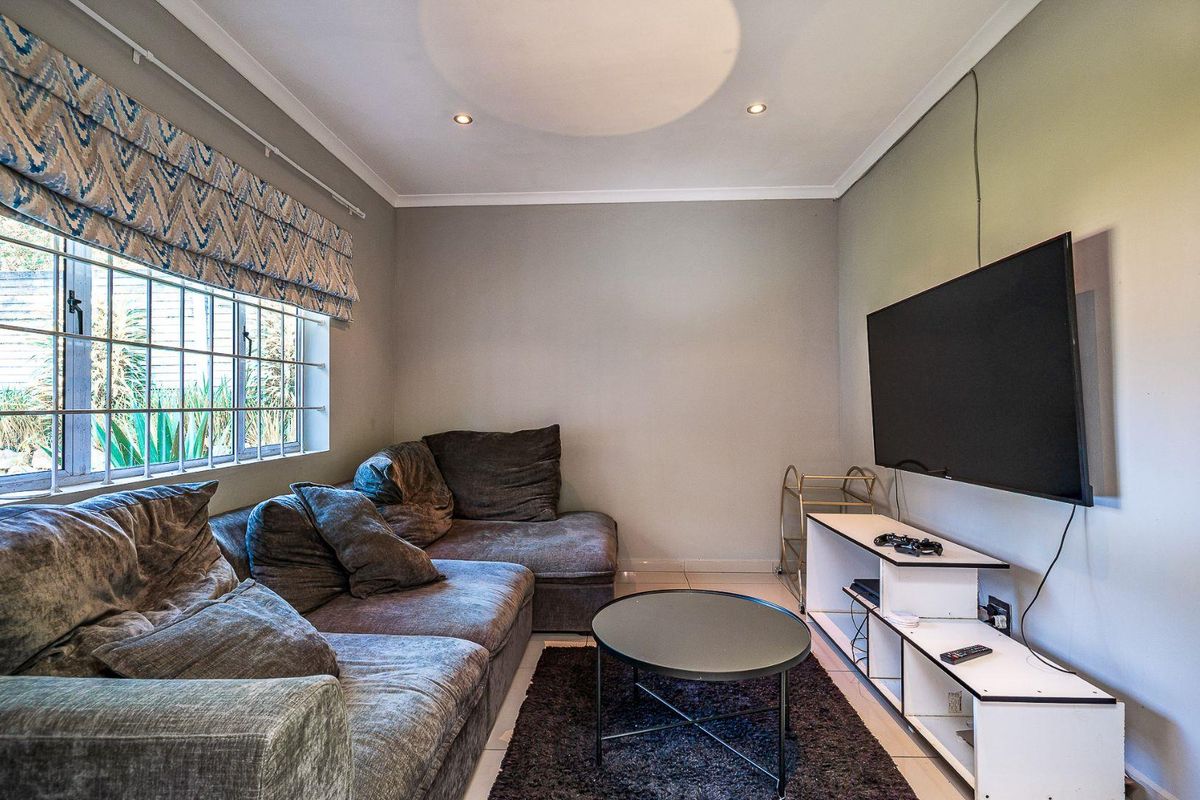 A cozy living room featuring tiled flooring, recessed ceiling lighting, and a window with a fitted roman blind.