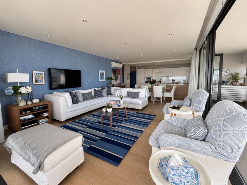 Spacious open-plan living and dining area featuring timber flooring, recessed lighting, a textured feature wall, and seamless access to the balcony.
