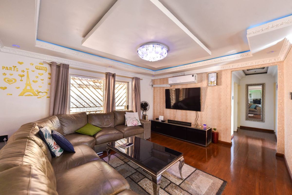 A well-maintained living room featuring a decorative tray ceiling with cove lighting, hardwood flooring, and a wall-mounted air conditioning unit.