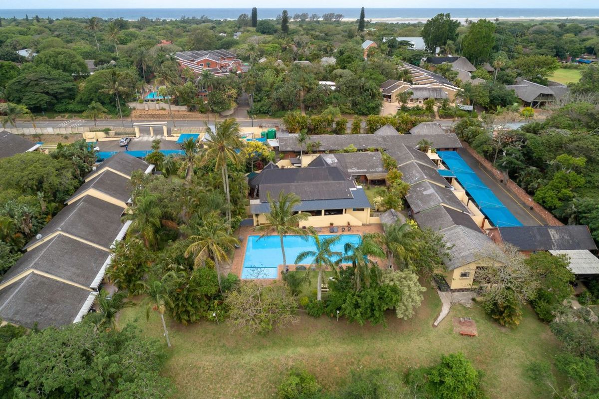 Aerial view of the apartment complex featuring a central swimming pool, landscaped grounds, and covered parking areas within a lush coastal setting.