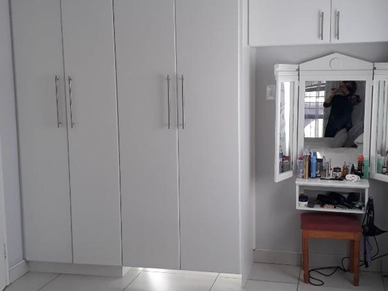 A bedroom featuring white built-in cupboards with overhead storage cabinets and neutral tiled flooring.