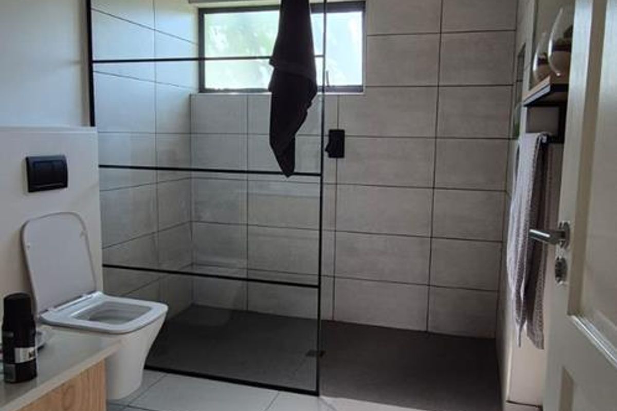 Modern bathroom featuring a walk-in shower with black frame, large format wall tiles, and a wall-mounted toilet.