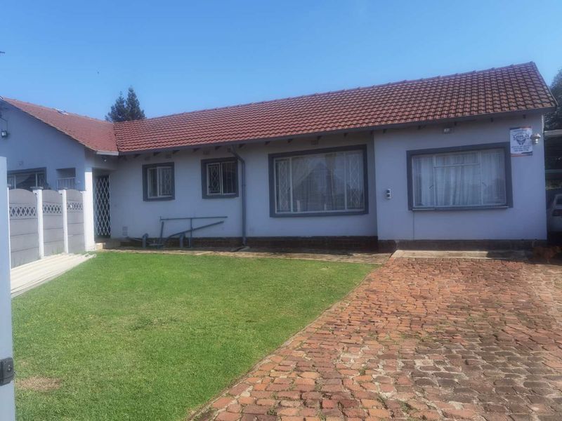 Front elevation of a single-story house featuring a tiled roof, brick paved driveway, and a well-maintained lawn area.