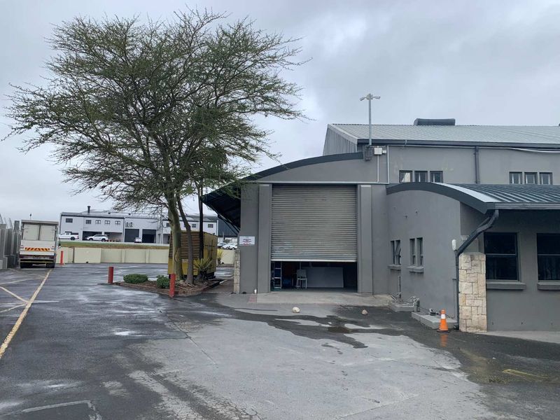Industrial property exterior featuring a large roller shutter door, concrete driveway, and stone-clad accents on a grey painted facade.