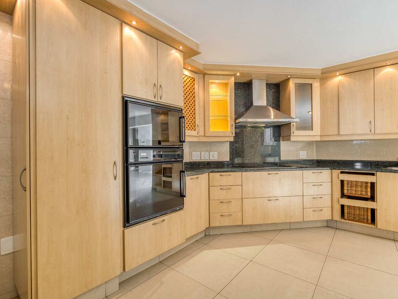 A well-maintained kitchen featuring light wood cabinetry, granite countertops, integrated appliances, and tiled flooring with recessed lighting.