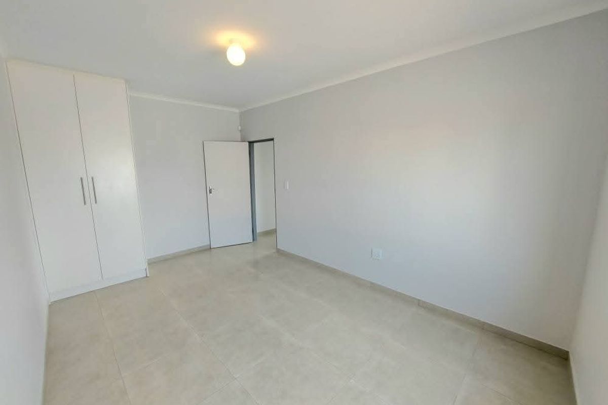 A bright, empty bedroom featuring neutral tiled flooring, built-in cupboards, and a clean, minimalist aesthetic ready for personalization.
