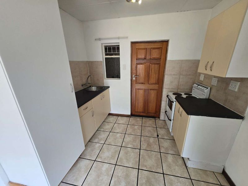 A functional kitchen featuring built-in cabinetry, laminate countertops, a stainless steel sink, and a freestanding stove with tiled flooring and splashbacks.