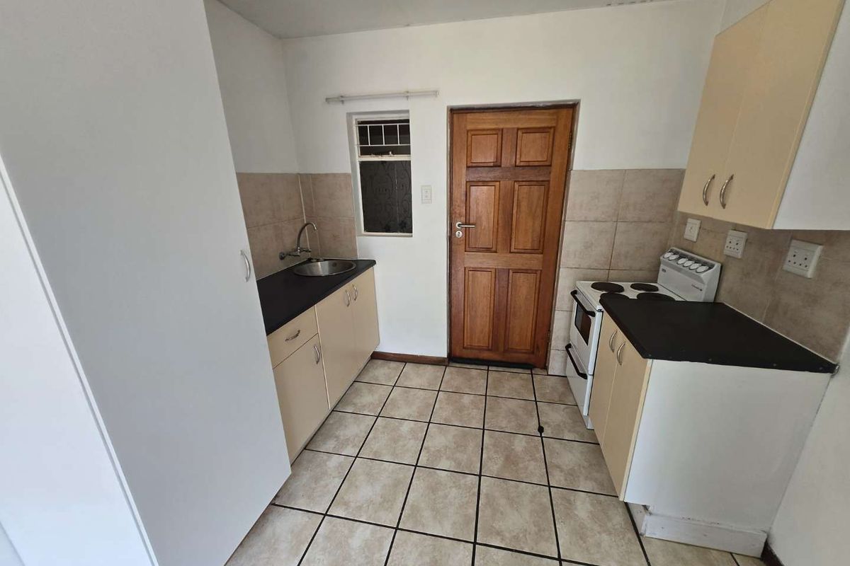 A functional kitchen featuring built-in cabinetry, laminate countertops, a stainless steel sink, and a freestanding stove with tiled flooring and splashbacks.