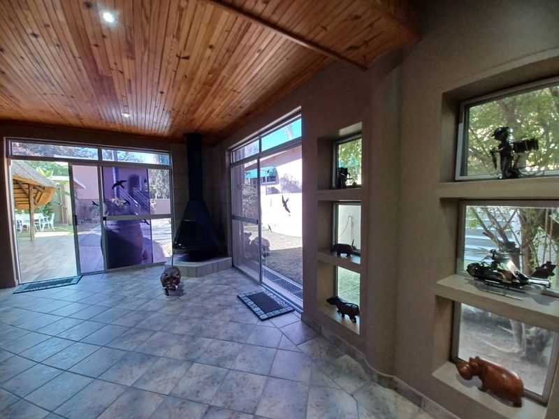 Spacious living area featuring a wood-paneled ceiling, tiled floors, a freestanding fireplace, and large sliding glass doors opening to the garden.