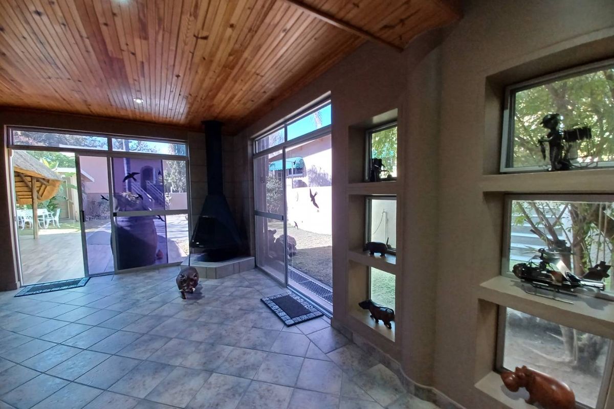 Spacious living area featuring a wood-paneled ceiling, tiled floors, a freestanding fireplace, and large sliding glass doors opening to the garden.