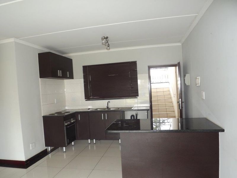 A clean, modern kitchen featuring dark cabinetry, granite countertops, built-in oven and hob, and tiled flooring, with direct access to an external staircase.
