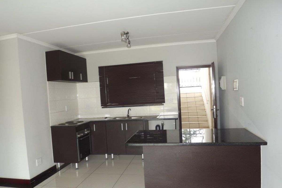A clean, modern kitchen featuring dark cabinetry, granite countertops, built-in oven and hob, and tiled flooring, with direct access to an external staircase.