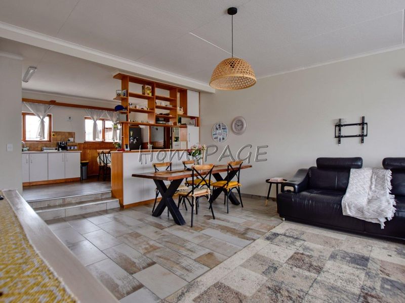 Open-plan living and dining area featuring tiled floors, a raised kitchen platform, and a timber room divider, creating a functional and connected living space.
