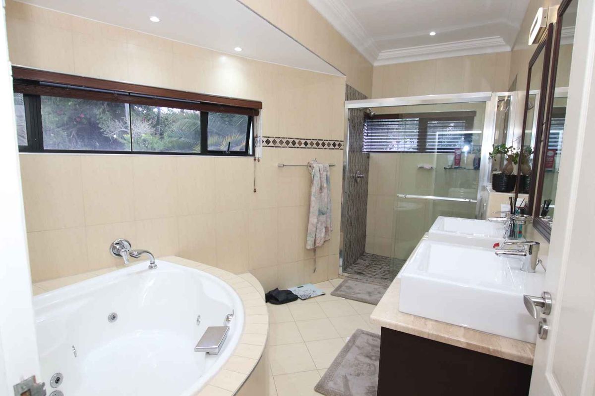 Spacious bathroom featuring a corner spa bath, glass-enclosed shower, and a double vanity with modern fixtures and neutral tiling.