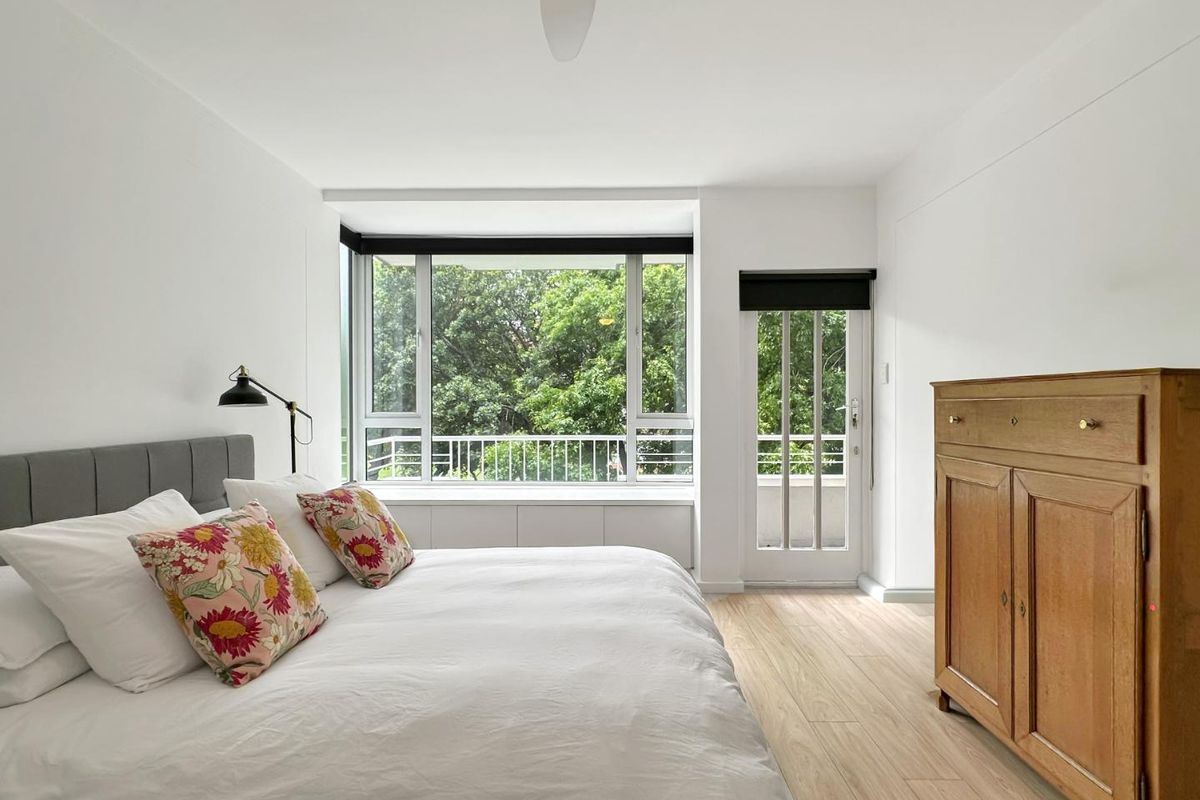 Bright bedroom featuring timber-look flooring, a built-in window seat, ceiling fan, and direct access to a balcony through a glass panel door.