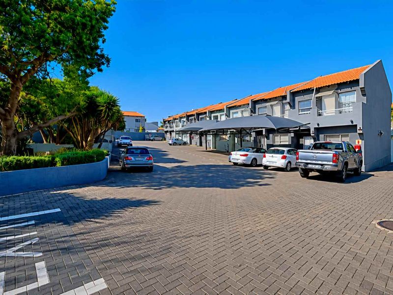 Exterior view of a townhouse complex featuring a paved driveway, covered parking bays, and well-maintained building facades with terracotta roof tiles.