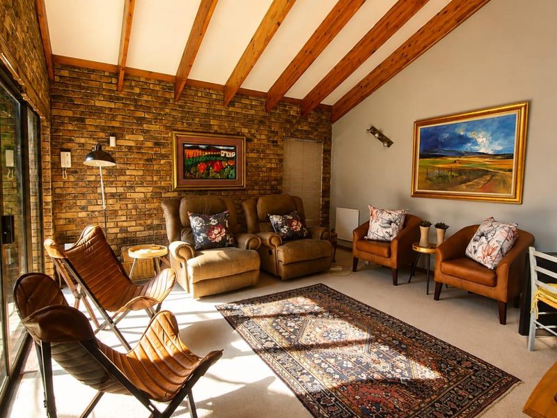 A cozy living room featuring exposed timber ceiling beams, a rustic brick feature wall, and large sliding glass doors providing natural light.