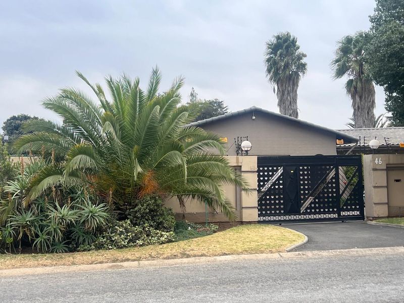 Front elevation of the property featuring a secure electric gate, perimeter wall with electric fencing, and a paved driveway.