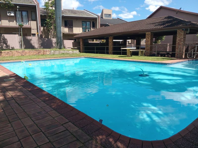 Communal swimming pool area featuring a paved surround and a covered brick patio structure for outdoor relaxation.