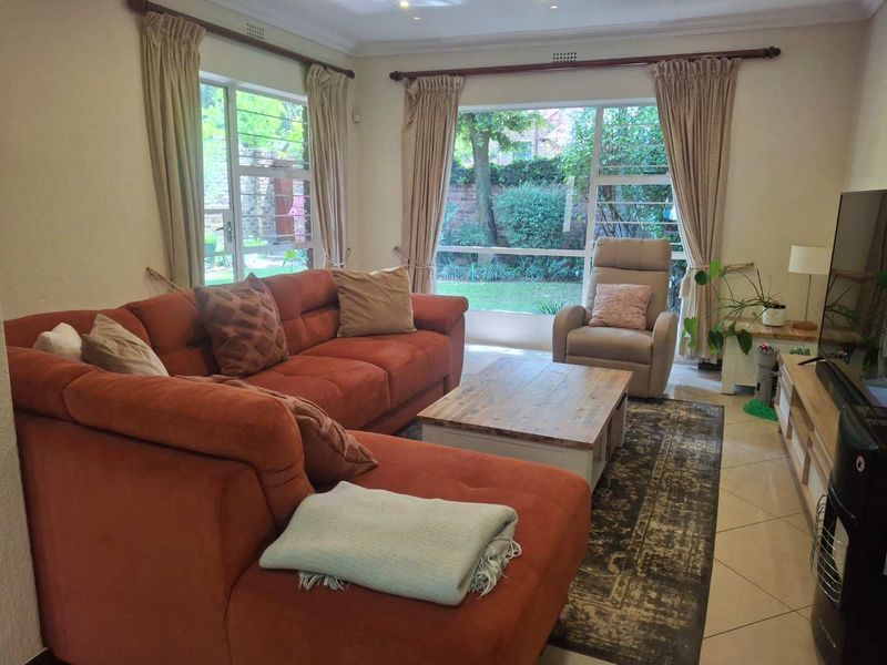 A comfortable living room featuring tiled flooring, recessed ceiling lights, and large windows providing views of the garden.