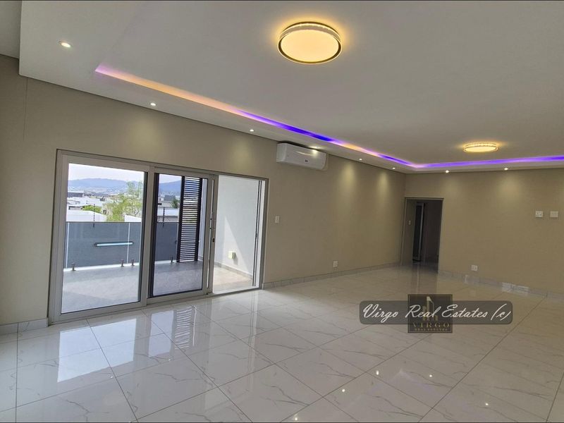 Spacious, modern living area featuring polished porcelain tiles, recessed ceiling lighting with LED accents, and sliding glass doors leading to an outdoor balcony.