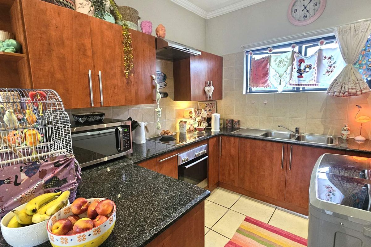 A functional kitchen featuring wood-finish cabinetry, granite countertops, a built-in oven, hob, extractor fan, and a double-basin sink with tiled splashbacks.