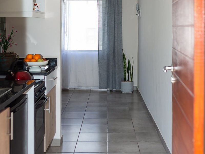A functional kitchen featuring built-in cabinetry, stone countertops, and ceramic floor tiles, leading to a bright windowed area.