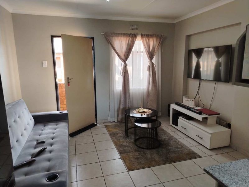 A functional living room featuring tiled flooring, neutral wall finishes, and direct access to an outdoor area.
