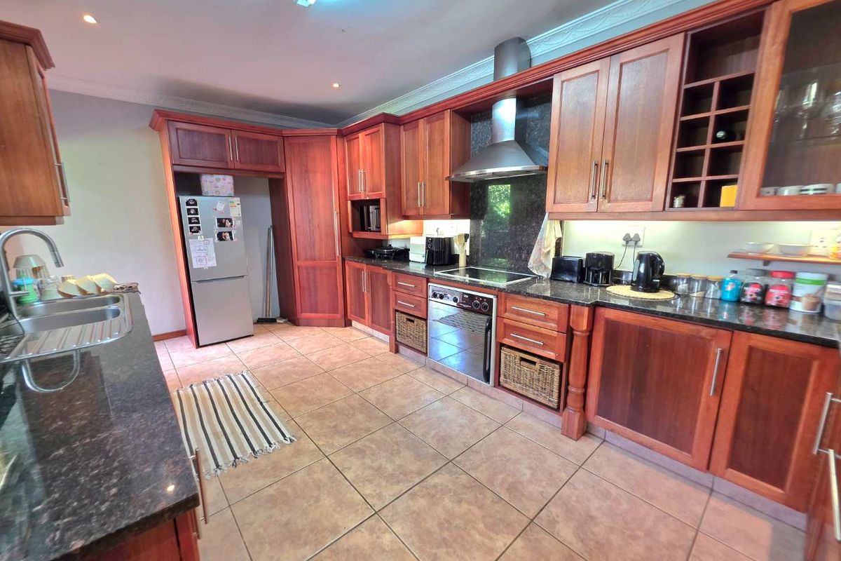 Spacious kitchen featuring warm-toned wooden cabinetry, granite countertops, a built-in oven, extractor fan, and tiled flooring.